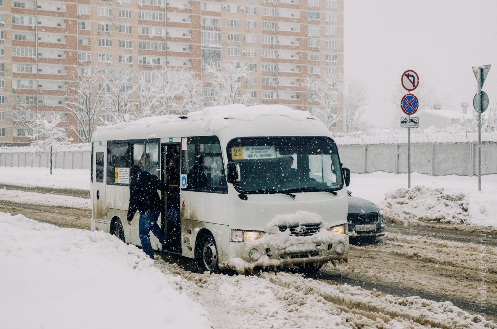 Белый микроавтобус, маршрутное такси, высаживает пассажиров на заснеженной остановке
