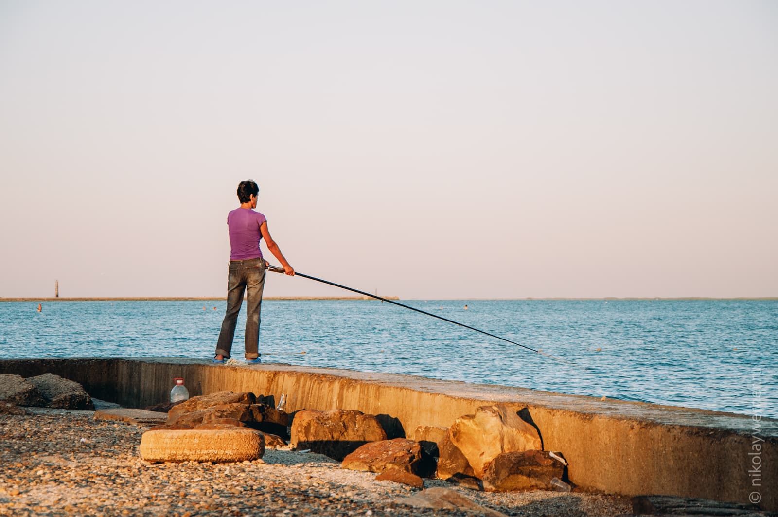 Женщина рыбачит, стоя на бетонном укреплении берега