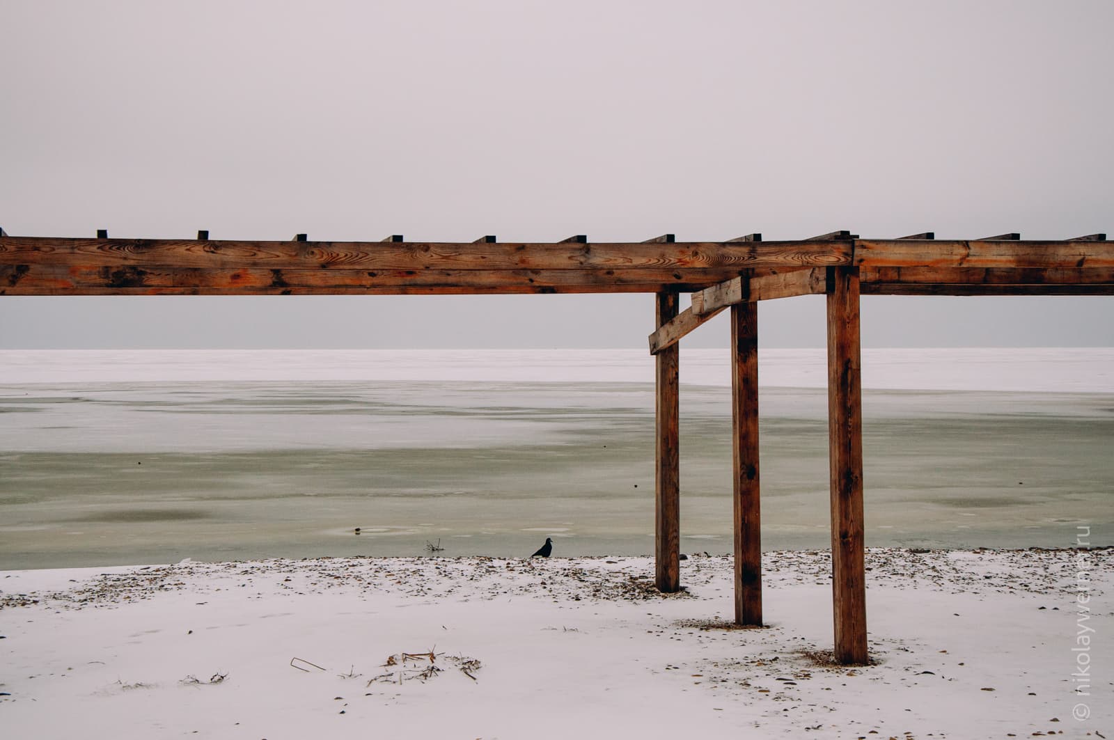 Берег моря. Каменистый пляж, укрытый тонким слоем снега. Стоит деревянный навес.