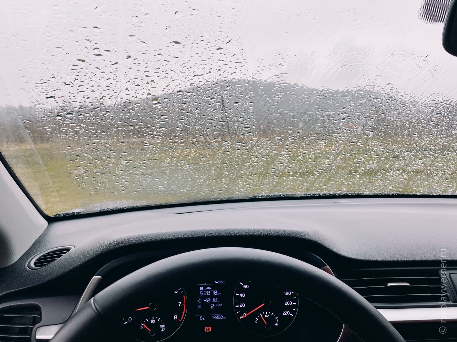 Фото из за руля авто. Сквозь залитое дождём ветровое стекло просматриваются силуэты гор
