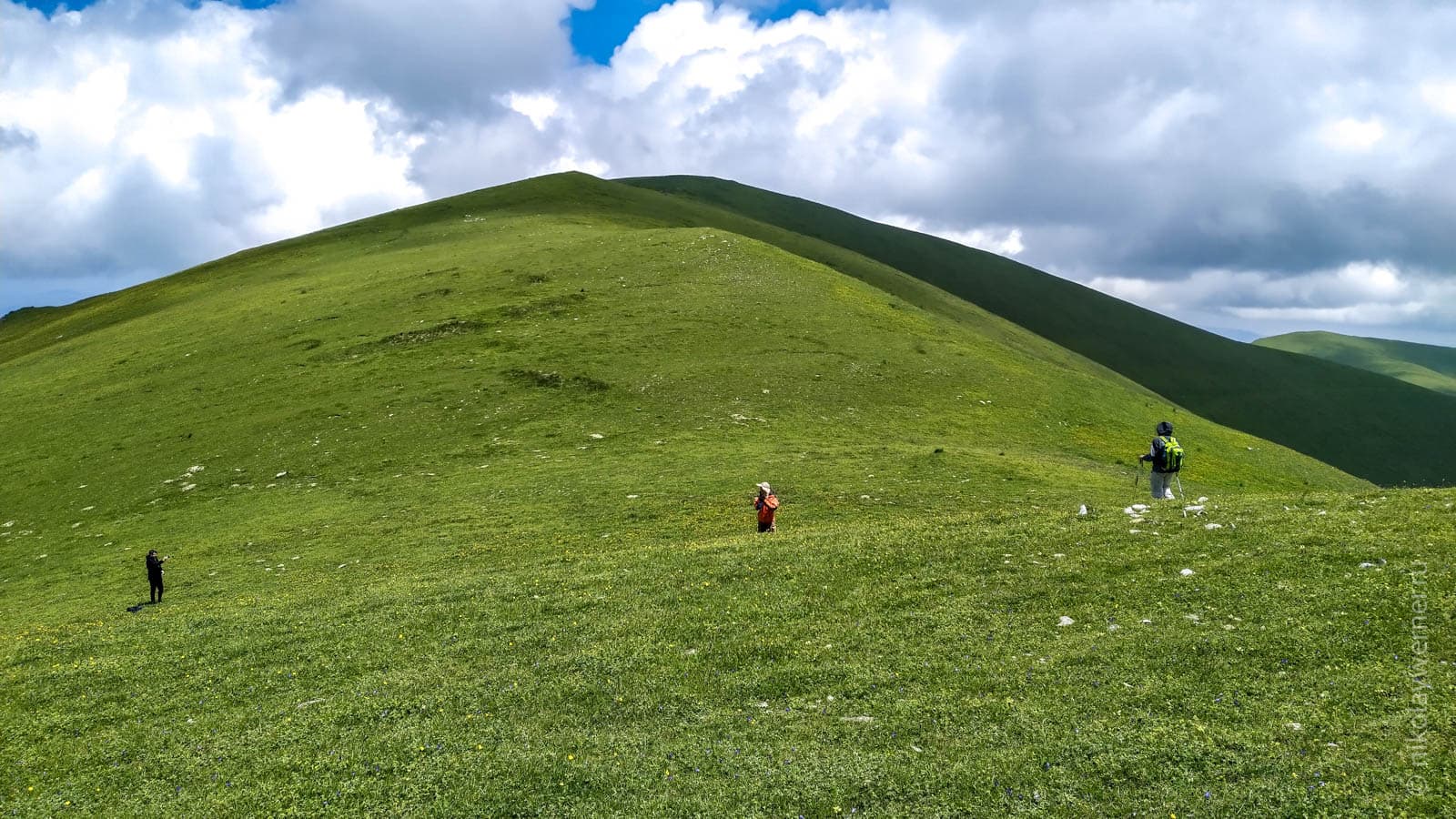 Трое туристов в отдалении среди зеленых холмистых вершин