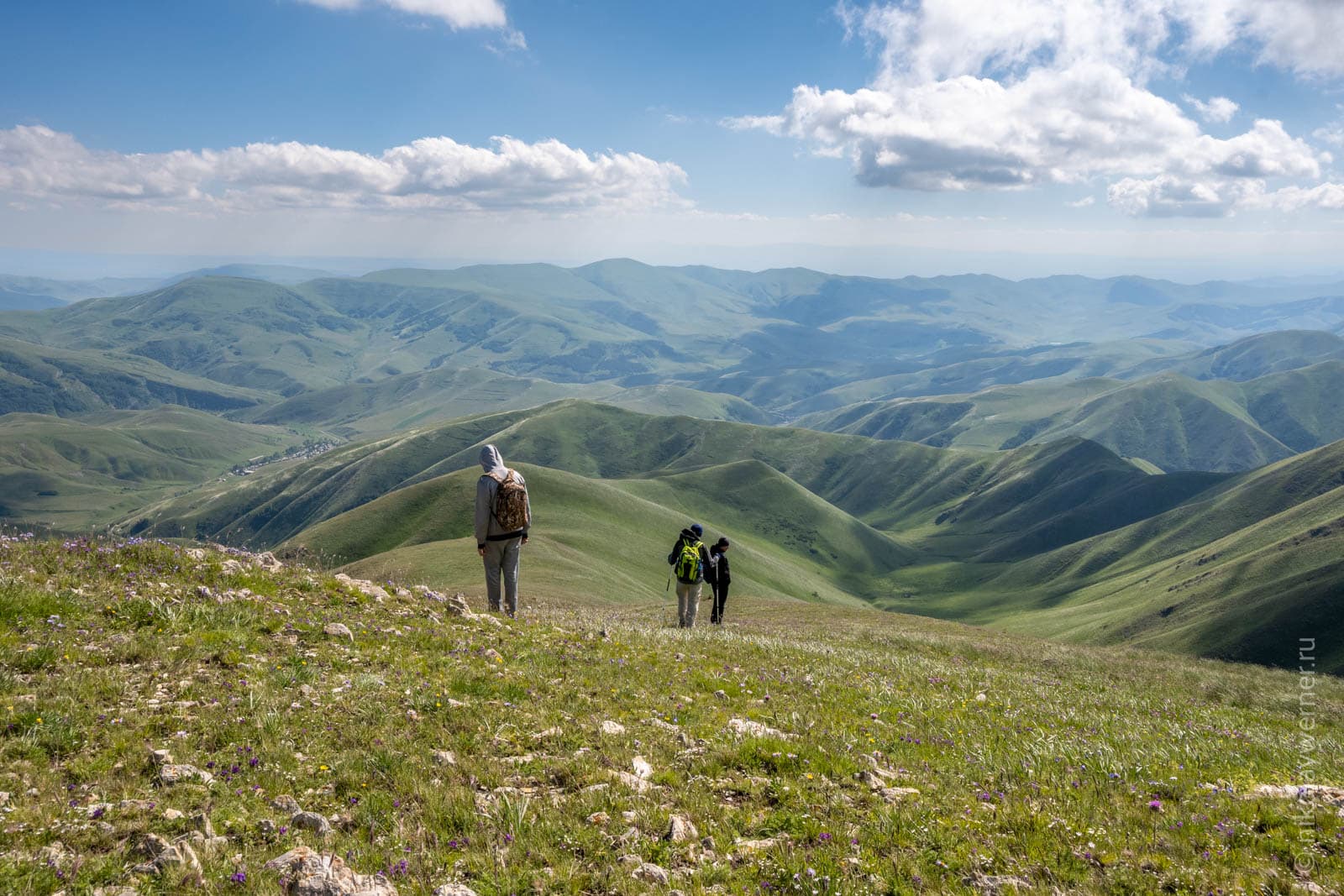 Три человека на склоне и зеленые складчатые горы далеко внизу
