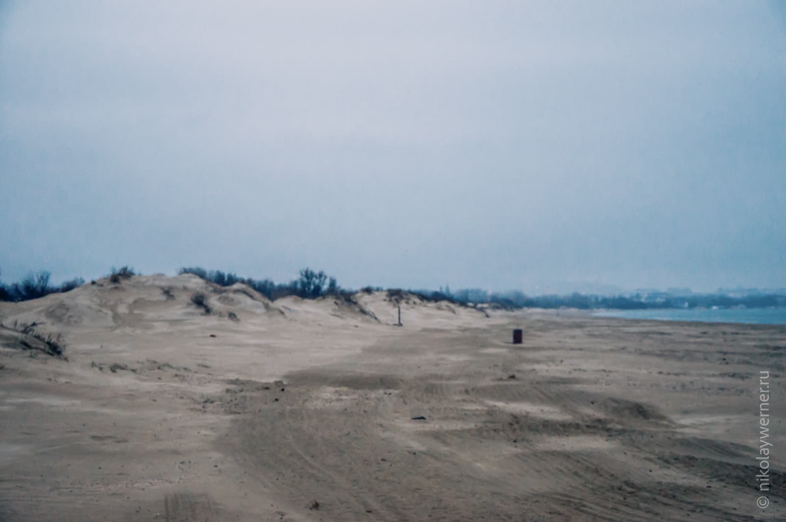Песчаный пляж с дюнами слева уходит вдаль. Справа виден кусочек моря. Пасмурно