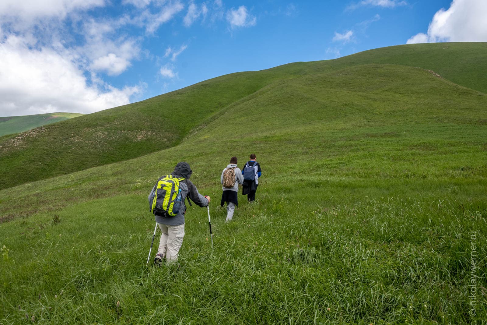 Группа туристов поднимается покрутому, укрытому травой, равномерно зеленому склону